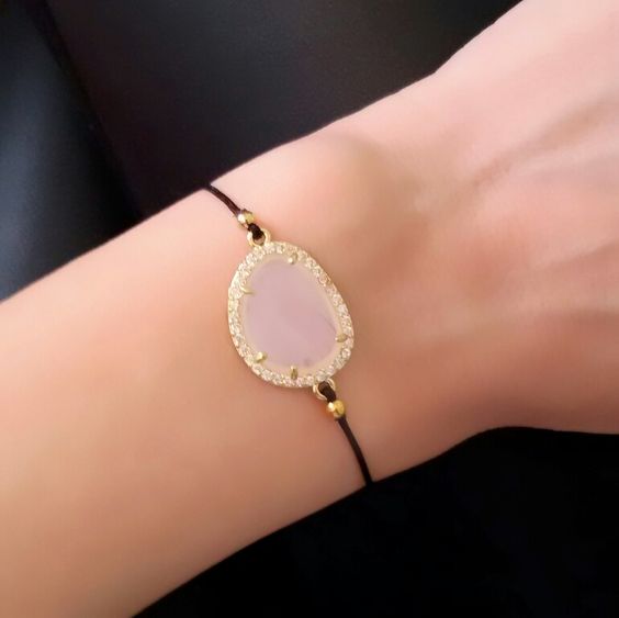 Bracelets femmes cordon coton 1 Bracelet argenté avec un pendentif en forme de goutte en pierre de quartz rose entourée de cristaux scintillants, sur un cordon noir élégant, parfait pour un style féminin et sophistiqué.