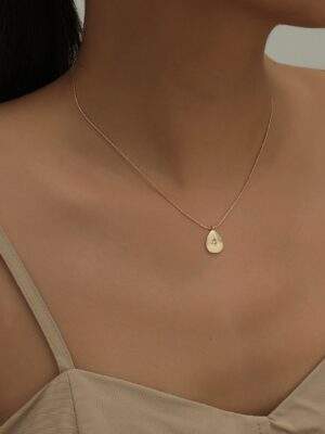 Collier fin en or rose avec pendentif en forme de goutte d'eau et petite étoile scintillante, porté sur un décolleté nu. Parfait pour un look élégant et discret, idéal pour toutes les occasions.